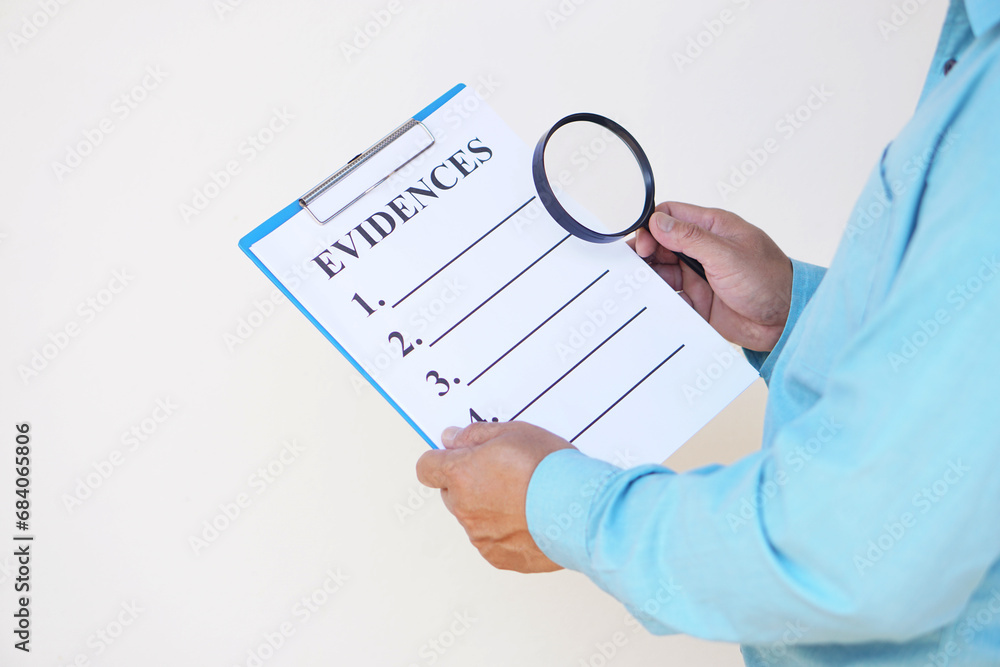 Close up a detective hold paper notepad clipboard with text EVIDENCES and magnifying glass. Concept, crime investigation to find criminal evidences. Close up a detective hold paper notepad clipboard with text EVIDENCES and magnifying glass. Concept, crime investigation to find criminal evidences.