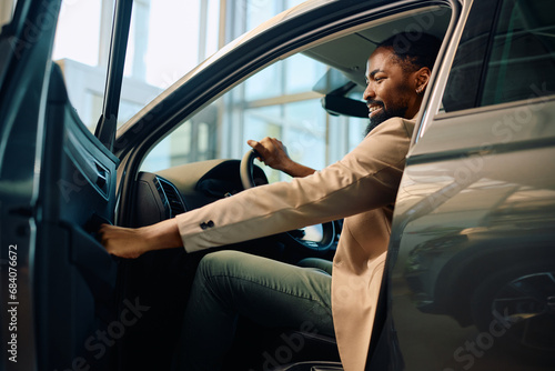 Konstfotografi Happy African American man getting inside of his new car after buying them in showroom