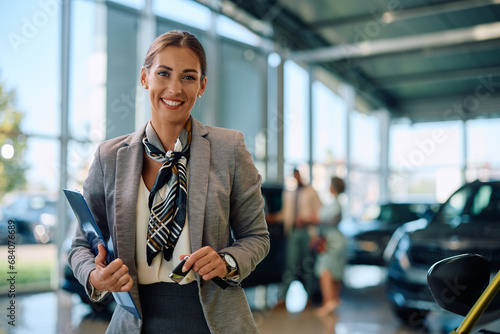 Portrait of happy car saleswoman in showroom looking at camera.