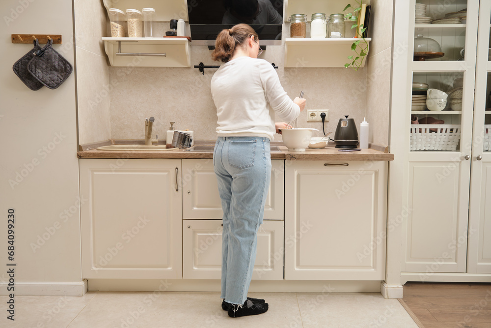 Back view of woman standing in modern kitchen and cooking pancakes Back view of woman standing in modern kitchen and cooking pancakes