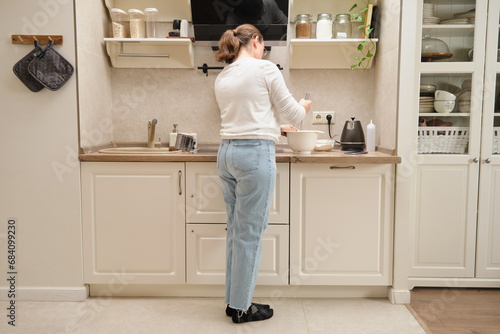 Back view of woman standing in modern kitchen and cooking pancakes