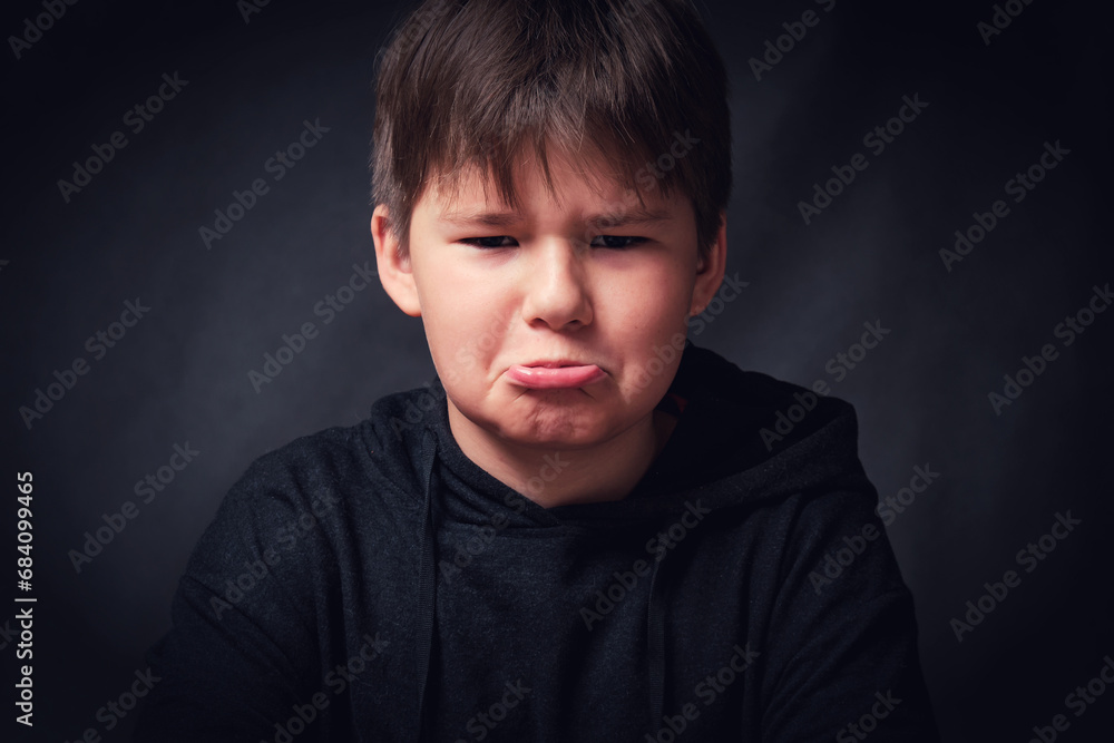 Fototapeta premium Little boy making funny sad faces on dark background. Closeup portrait of cute kid