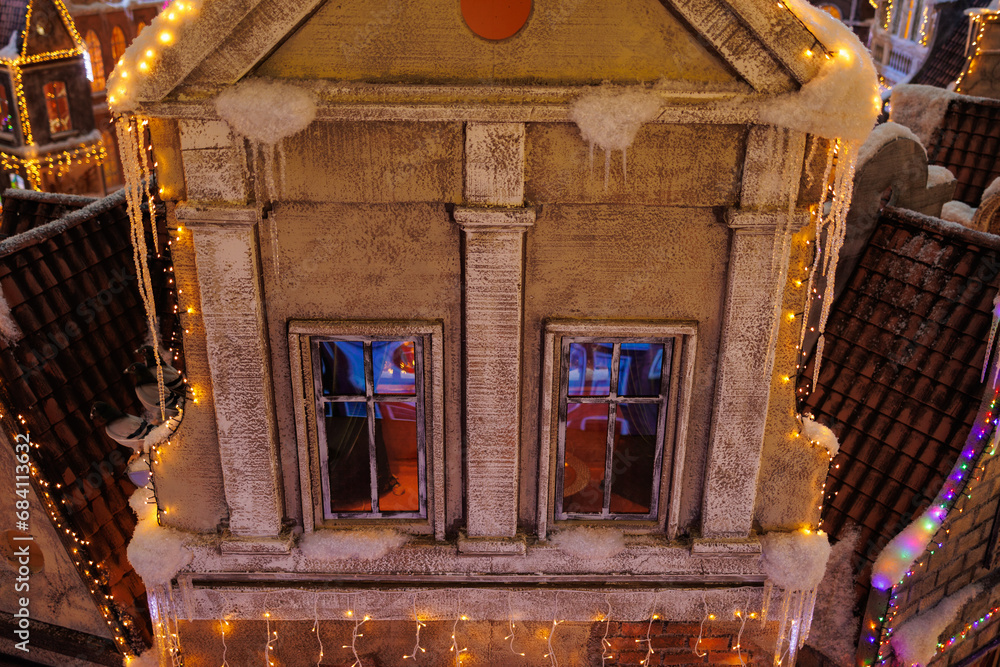 Fototapeta premium New Year's decorations, toys and garlands on the windows in fabulous scenery. Houses for children in a public place. 