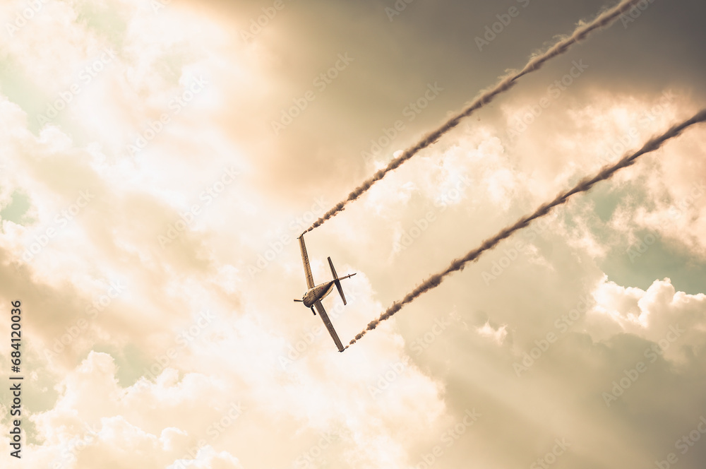 Obraz premium Airplane leaving smoke behind and flying against the sky at sunset.