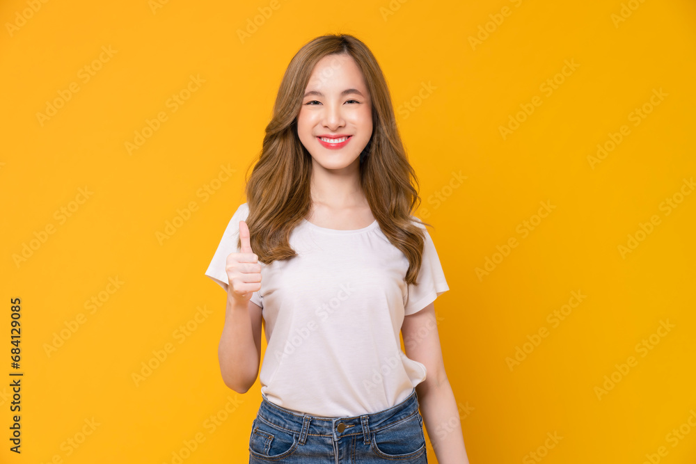 Studio shot of cheerful beautiful Asian woman in white t-shirt and showing thumbs up or like on yellow background. Studio shot of cheerful beautiful Asian woman in white t-shirt and showing thumbs up or like on yellow background.