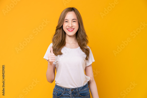 Studio shot of cheerful beautiful Asian woman in white t-shirt and showing thumbs up or like on yellow background. photo