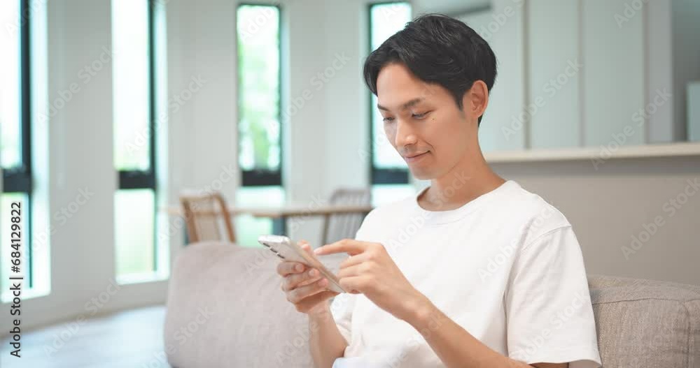 ソファに座ってスマートフォンを操作する男性 ソファに座ってスマートフォンを操作する男性