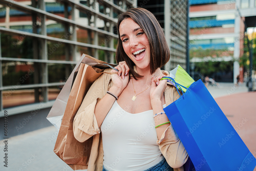 Close up portrait of a young woman holding shopping bags and looking excited at camera. Joyful customer female enjoying a discount purchase. Lady smiling buying a retail. Buyer girl at sale store Close up portrait of a young woman holding shopping bags and looking excited at camera. Joyful customer female enjoying a discount purchase. Lady smiling buying a retail. Buyer girl at sale store