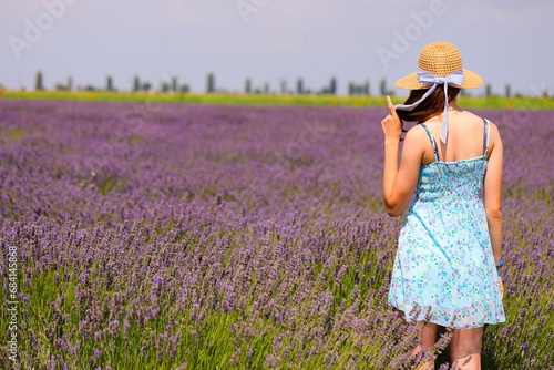 young girl with straw hat and short dress points in the middle of the lavender field in bloom