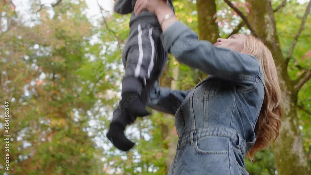 Happy blonde mom playing with baby throwing him in air walking in autumn park. Mother enjoying time with kid. Maternity leave, raising child, baby care in family, happy babyhood with mommy concept. Happy blonde mom playing with baby throwing him in air walking in autumn park. Mother enjoying time with kid. Maternity leave, raising child, baby care in family, happy babyhood with mommy concept.