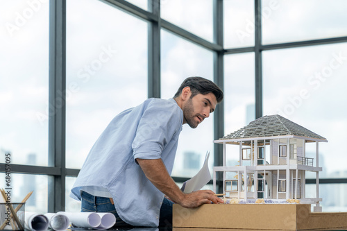 Professional caucasian architect engineer inspect modern house model with skyscraper view while comparing between house model and blueprint with project plan and architectural equipment. Tracery.