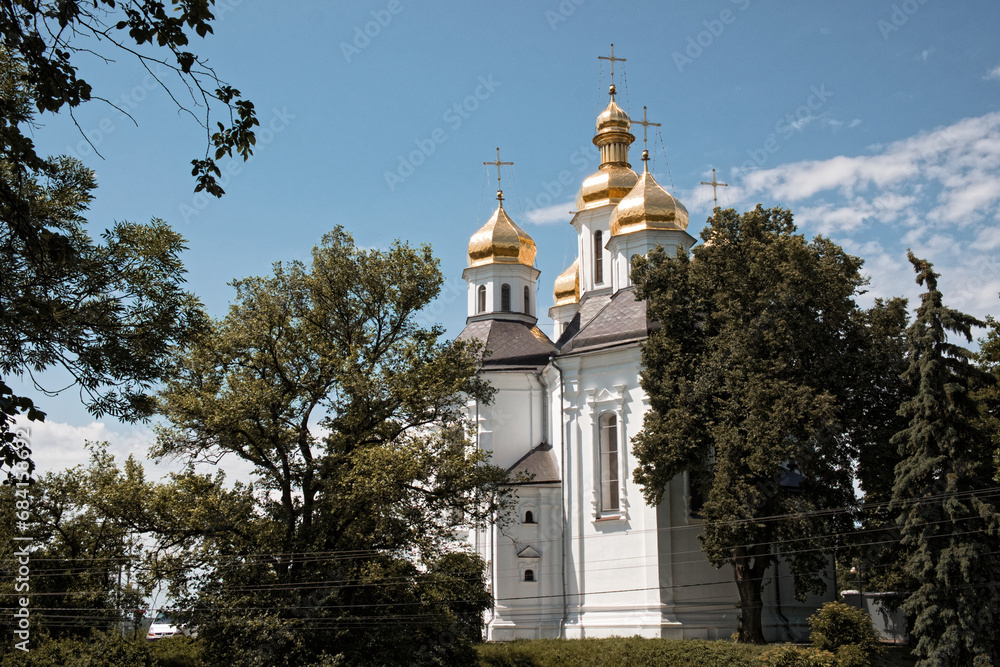 A church with golden domes and crosses on top, surrounded by trees. Catherine's Church. The Orthodox Church in the Ukrainian city of Chernigov, an architectural monument of national importance.