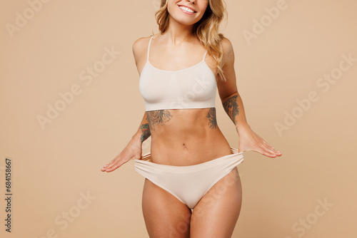 Close up elegant young nice lady woman with slim body perfect skin wears nude top bra lingerie stand hold hand on panties isolated on plain pastel light beige background. Lifestyle diet fit concept.