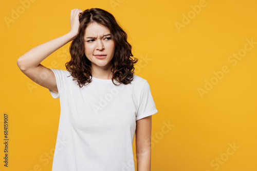 Young sad mistaken confused Caucasian woman she wear white blank t-shirt casual clothes scratch head look aside on area isolated on plain yellow orange background studio portrait. Lifestyle concept.
