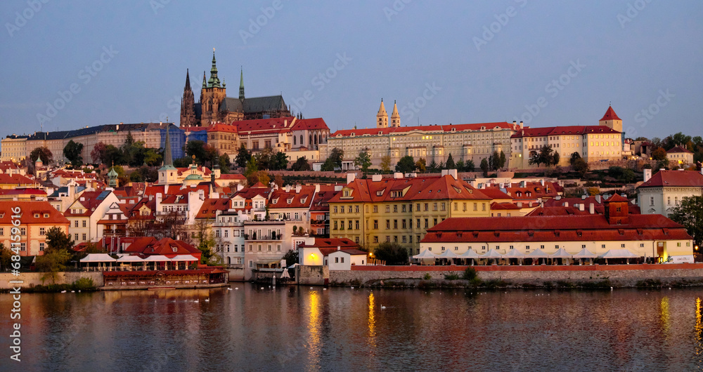 Prague Castle on a hill with surrounding buildings and river under a pinkish sky.