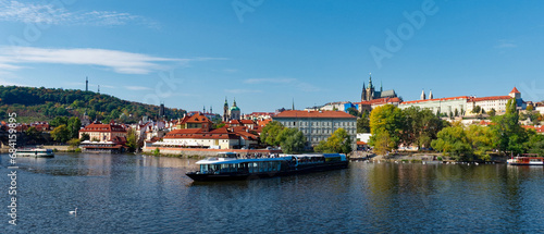 This is a photo of a river with a boat and buildings in the background. Pleasure boat on the Vltava pier in the fall. View of Prague.