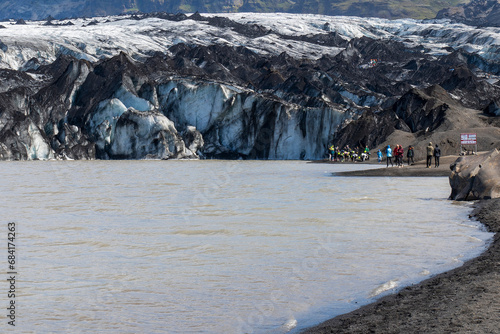 Tourists hiking near Solheimajokull Glacier, a glacier tongue of the Myrdalsjokull glacier.  The glacier covers the great Katla, an active volcano.  photo