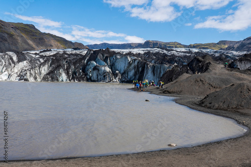 Tourists hiking near Solheimajokull Glacier, a glacier tongue of the Myrdalsjokull glacier.  The glacier covers the great Katla, an active volcano.  photo