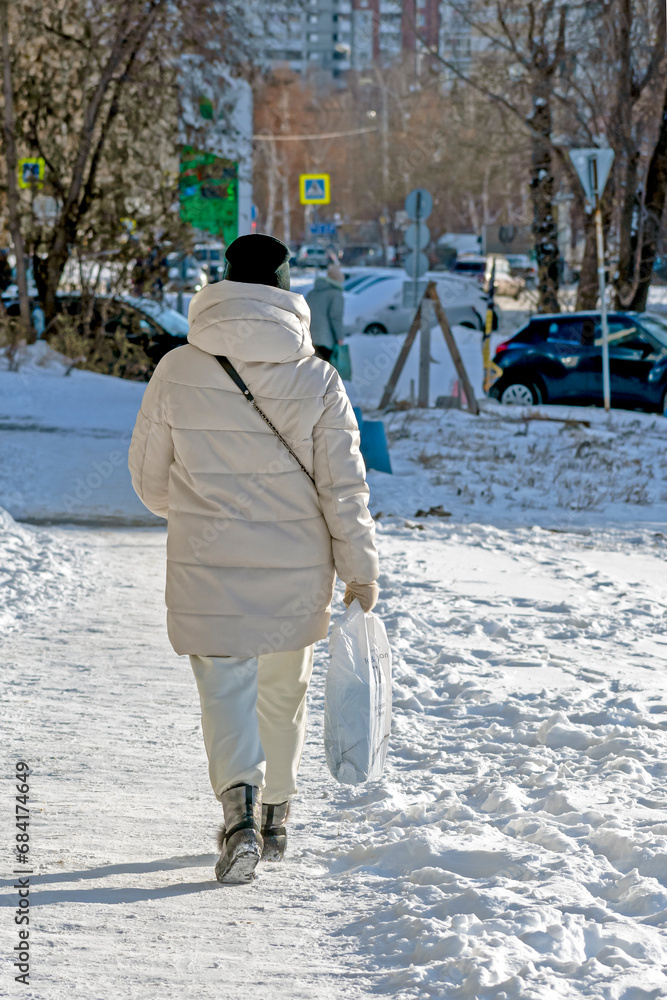 A woman walks on a snowy sidewalk on a winter day