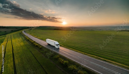white truck driving on asphalt road along the green fields at sunset seen from the air aerial view landscape drone photography cargo delivery © Enzo