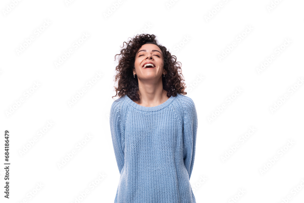 authentic smiling young brunette woman with curls is dressed in a blue knitted sweater on a white background authentic smiling young brunette woman with curls is dressed in a blue knitted sweater on a white background