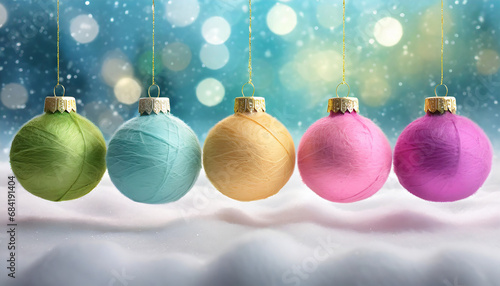 Coloured Christmas balls of wool hanging from golden strings above snowy ground with blurred background with sparkling lights and falling snow