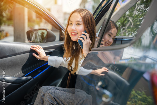 Confidence and technology blend as an Asian businesswoman sits in her car, talking on the phone. She's poised for success, with the open car door representing her active role in the business world.