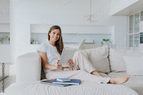 cheerful young woman in casual clothes sitting on the couch at home using tablet looking at camera smiling enjoying weekend home. A professional psychologist preparing for consultation via Internet