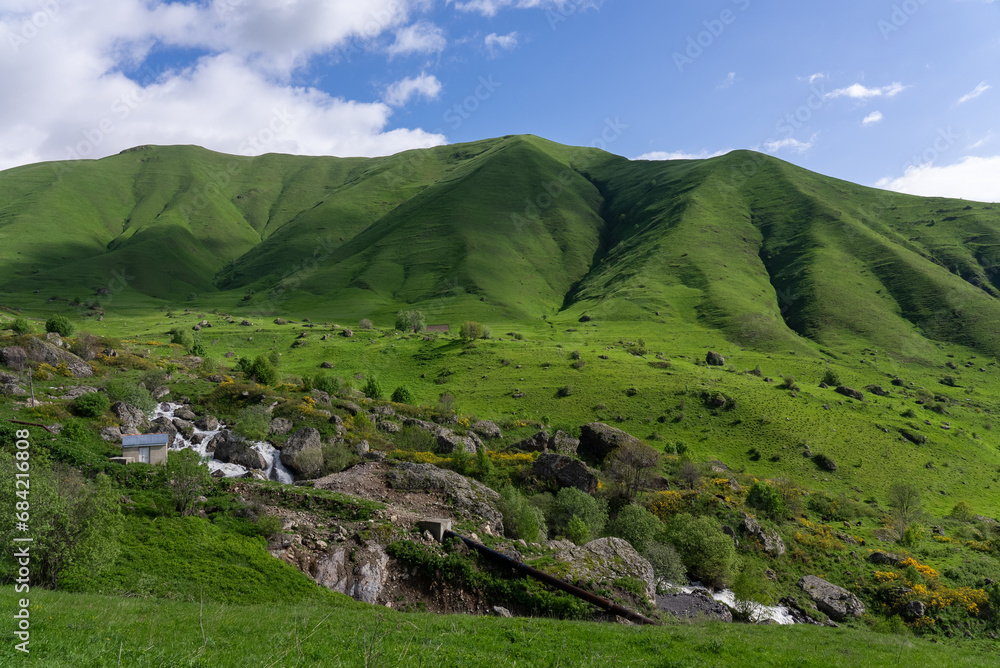 Fototapeta premium Landscape of Green Meadow on Mountains with Small Stream Under Blue Sky in Summer