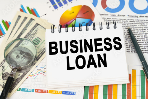 On the table are business charts, dollars and a notepad with the inscription - Business Loan