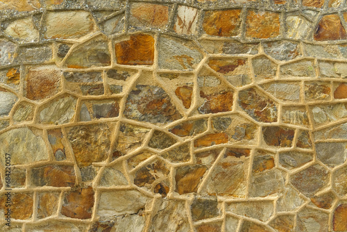 Old rough stone wall made of various square natural stones in beige, gray and brown colors.