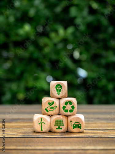 Eco friendly, green renewable energy icons on wooden cube block stack pyramid shape on green leaves background, vertical style. Environmental sustainability, Net zero carbon dioxide reduction concept.