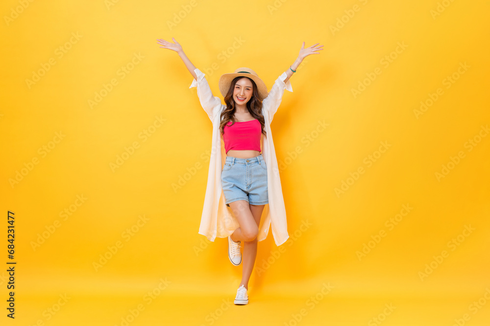 Full body portrait of pretty Asian woman wearing summer outfit smiling and raising hands up in colorful yellow isolated background studio shot Full body portrait of pretty Asian woman wearing summer outfit smiling and raising hands up in colorful yellow isolated background studio shot