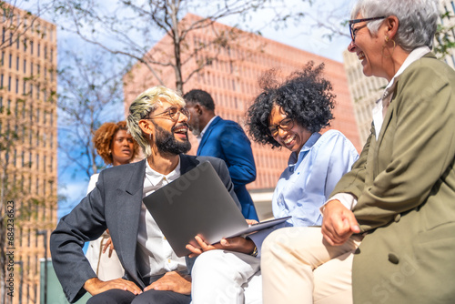 Smiling business team using laptop sitting outdoors in a bench