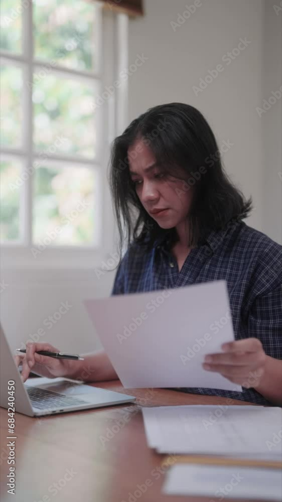 Midlife Asian woman working on her laptop in the living room at home on a leisure day Midlife Asian woman working on her laptop in the living room at home on a leisure day