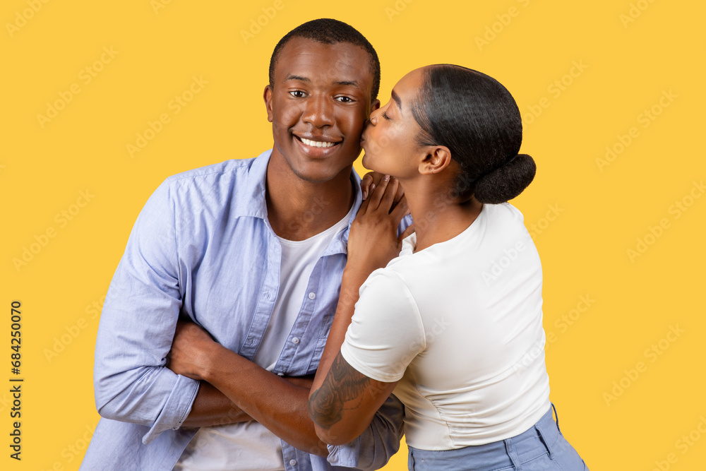 Black woman kissing man on cheek, he smiles at camera Black woman kissing man on cheek, he smiles at camera