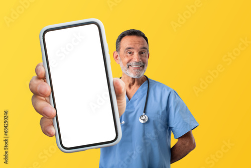 Mature medical worker man in uniform demonstrating smartphone screen, studio