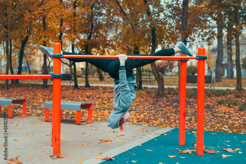 Young gymnast Caucasian woman at playground hanging upside down on bars and doing splits in park at autumn