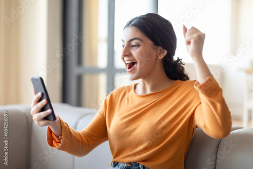 Excited Young Indian Woman Looking At Smartphone At Home And Celebrating Success