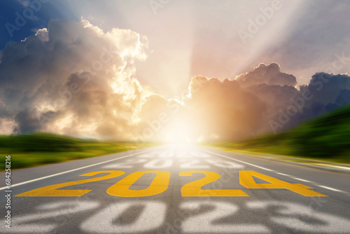 2024 New Year road trip travel and future vision concept. Number of the old year and New Year written on middle highway road in the empty asphalt road with sunset or sunrise light above asphalt road. photo