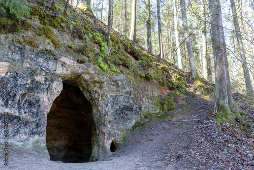 a rock cave in a wooded area with a walking path behind it