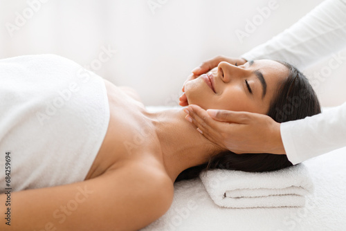 Relaxed young indian woman enjoying face lifting massage in spa