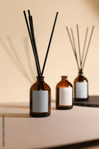 Focus on One Organic Essential Oil Diffuser Bottle with Wooden Sticks on a Background of 2 blurred bottles, Seamless Beige Brown Backdrop, Ready for Custom Labeling