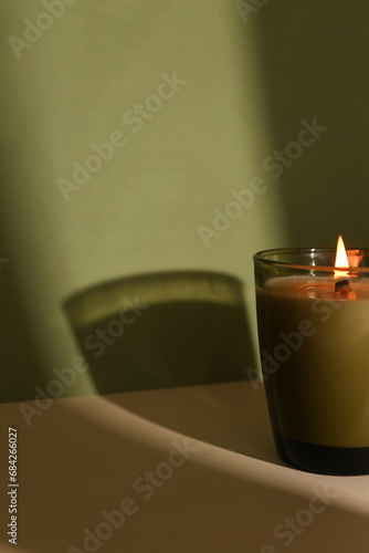 Burning Soy Organic Candle Amidst a Green Backdrop, Featuring an Empty Label for Personalized Customization and Infusing the Surroundings with Cozy Ambiance