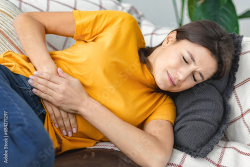 Foto Young woman suffering from abdominal pain lying on the couch at home