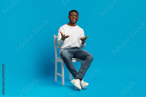 Confident handsome black guy sitting on chair, gesturing © Prostock-studio