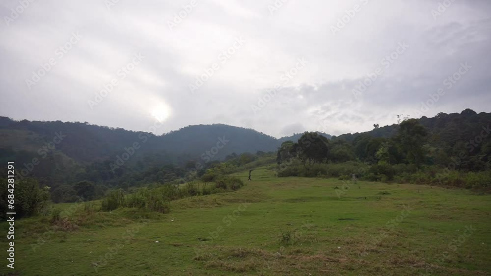 beautiful natural views of mountains, natural panorama of hills, and forests of tall green trees and slopes of green plants under cloudy blue skies during the day