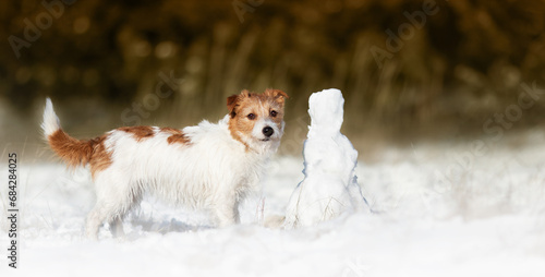 Cute happy dog listening in the snow with a snowman. Walking, hiking with pet in winter, christmas banner.