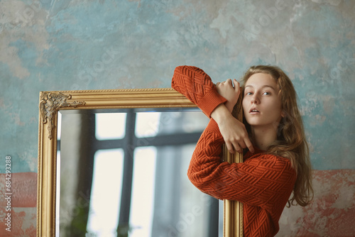 Dreamy young girl leaning on mirror in golden antique frame