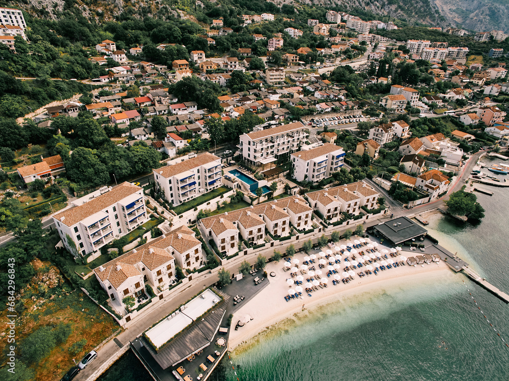Private beach with sun umbrellas near the Huma Kotor Bay Hotel. Dobrota, Montenegro. Drone